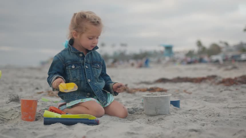 Blonde girl with jeans jacket playing with sand on the beach