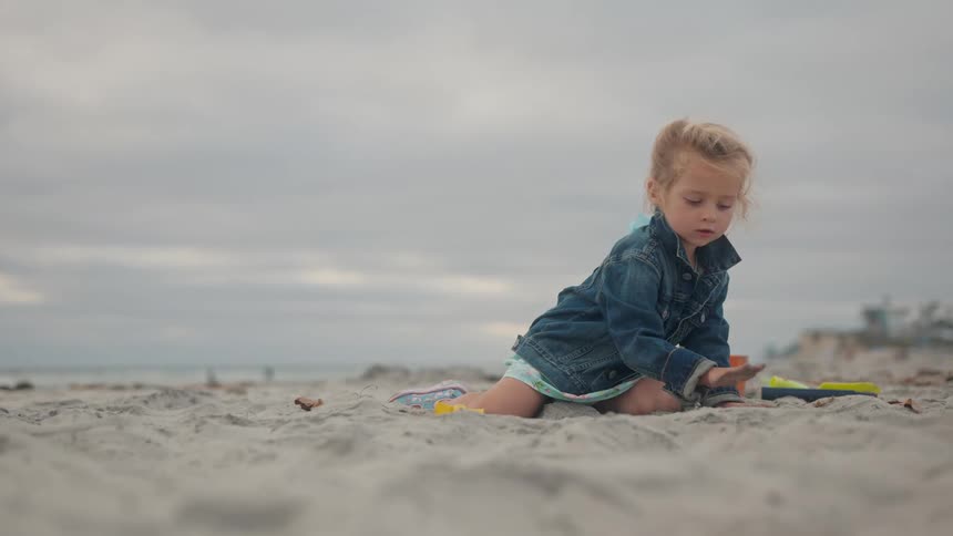 Blonde girl with jeans jacket playing with sand on a beach