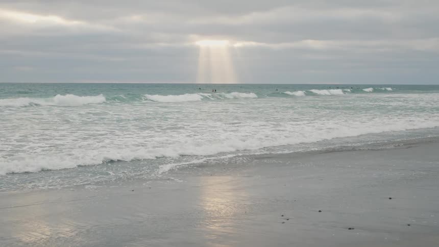 People swimming neckdeep in the ocean with sunlight peeking through the clouds at them