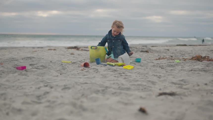 Blonde girl with jeans jacket playing with sand in the beach