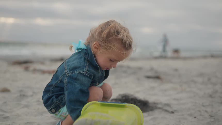 Little girl playing with sand on the beach on a cloudy day