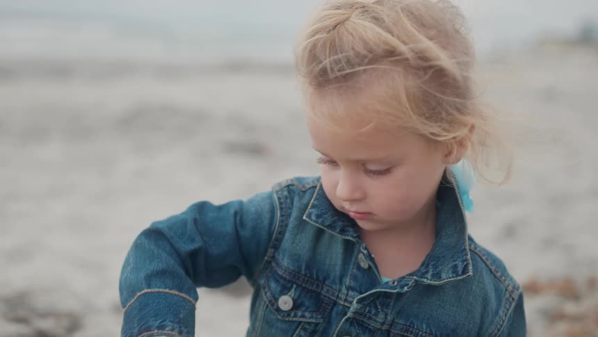 Little blonde girl playing in the sand on the beach