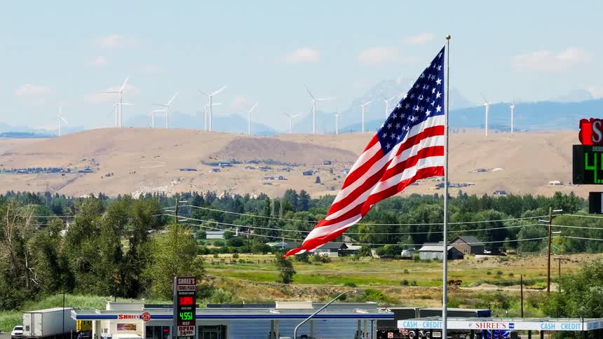 American flag in front of a gas station and wind turbines in the mountains in the background