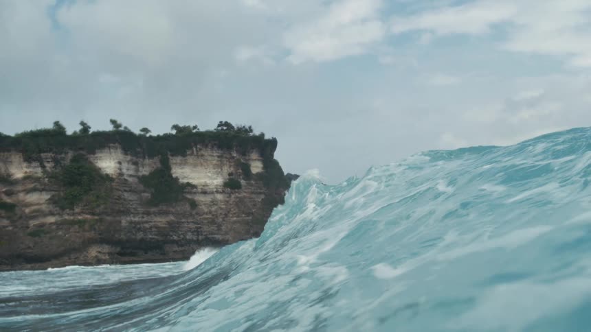 A wave forms and crashes on the ocean surface during daytime
