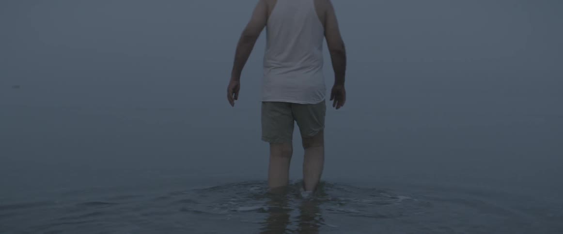 A man wades into a body of water on a foggy day