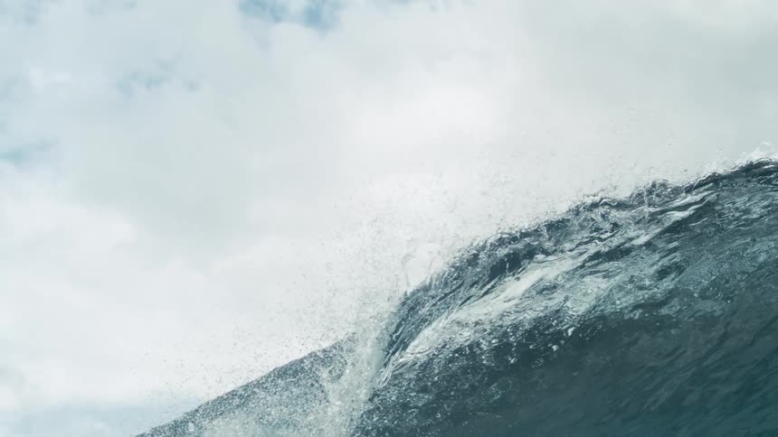 A dynamic shot of a large dark blue ocean wave cresting and breaking with white foam under an overcast sky