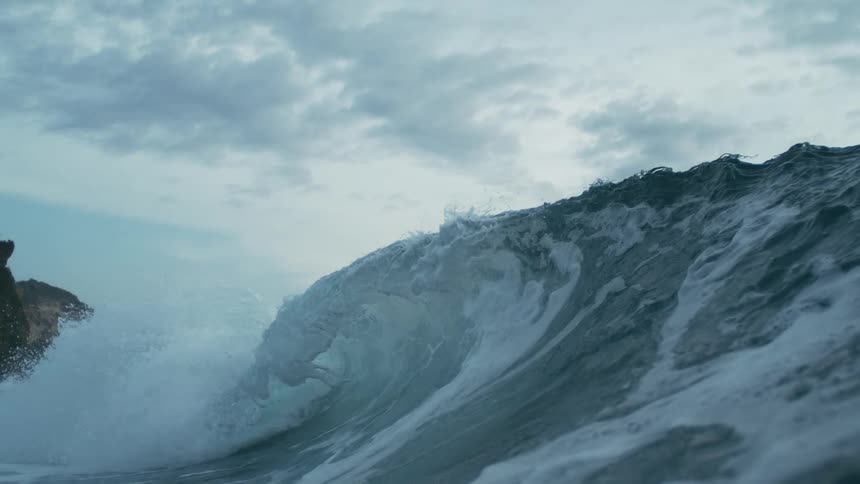A huge ocean wave forms and crashes along the ocean surface during daytime