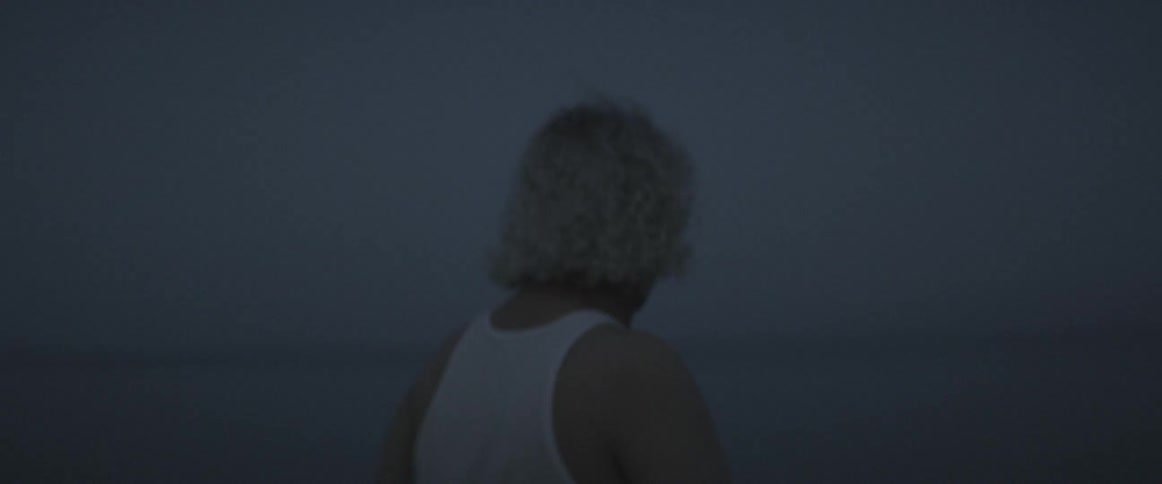 An older man with glasses walking along the coast in the evening