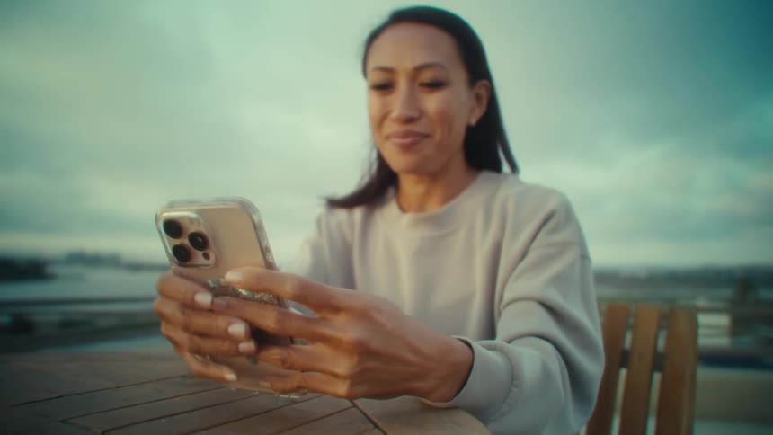 Woman smiles while using smartphone at outdoor table