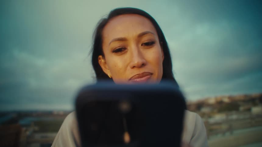A woman looks down at her phone slightly smiling as evening sunlight softens the background