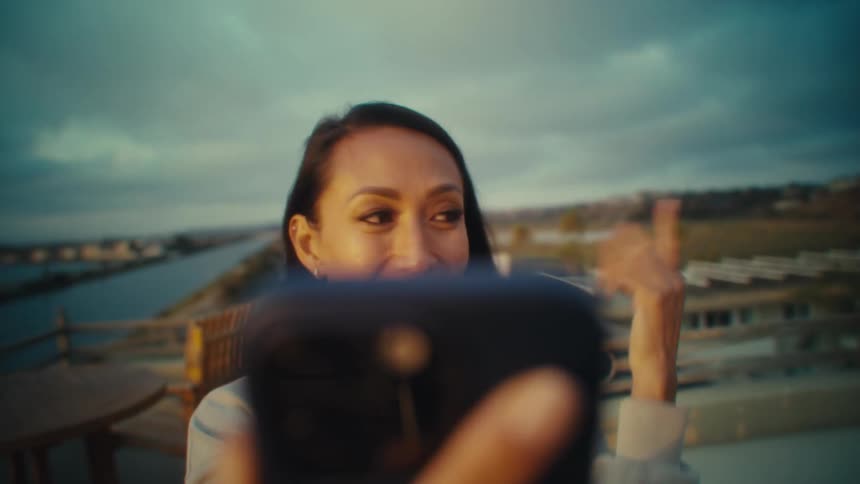 A young woman takes selfies with her phone while standing outdoors on top of a building during daytime