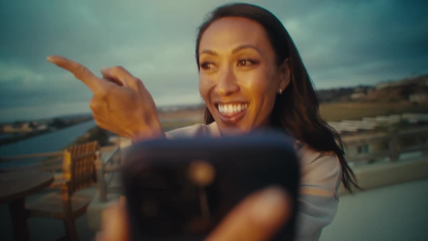 A woman joyfully gestures while taking a selfie outdoors at sunset