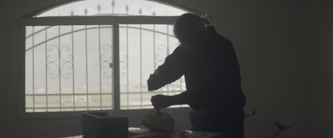 An elderly man works with a hammer and chisel