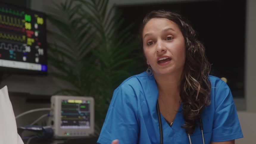 A nurse attentively explains something while seated beside medical equipment