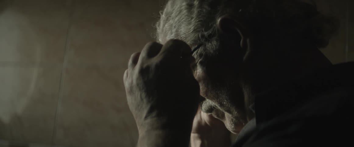 An elderly man puts on his glasses