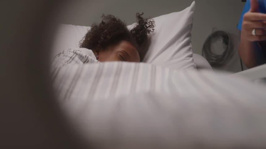 A closeup view of a person with curly hair lying in a bed with white pillows and striped sheets