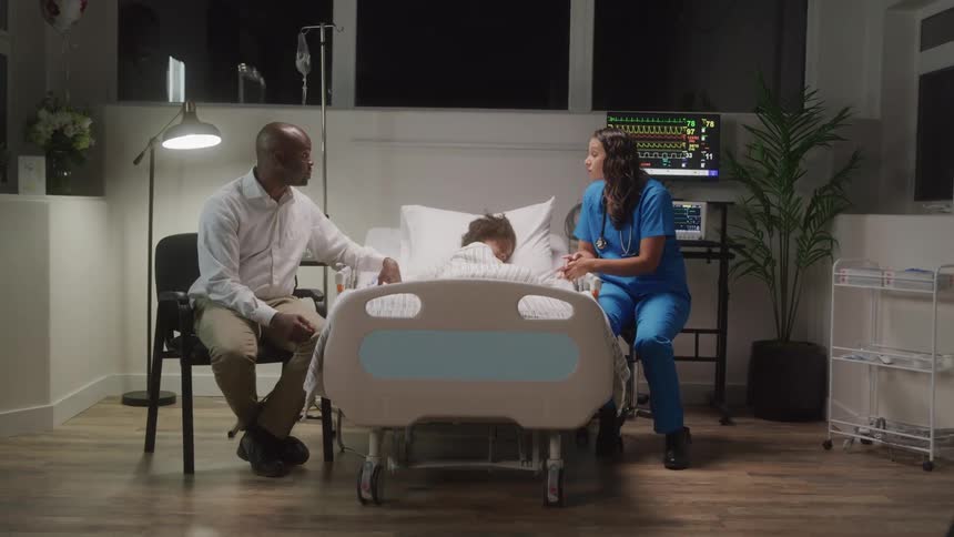 Nurse talks to the father of a child who is lying on a gurney in a hospital room at night