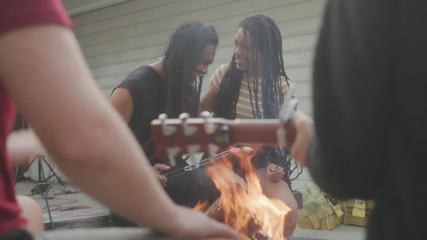 People playing guitar with happy expression around a campfire