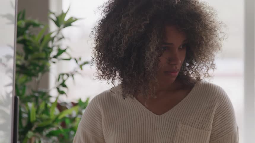 A woman with curly hair is shown intensely focused on writing on a whiteboard with a marker she pauses to look away possibly engaging with someone or contemplating her next thought