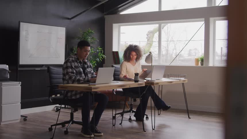 Two individuals one man and one woman are working indoor infront of laptops