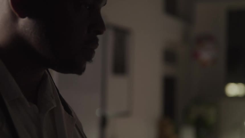 A doctor in a white lab coat stands with a serious expression looking down while a stethoscope hangs around his neck the lighting creates a somber mood around him