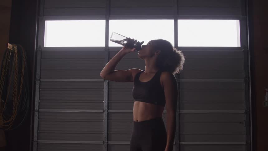 Woman in workout clothing drinking water in a garage