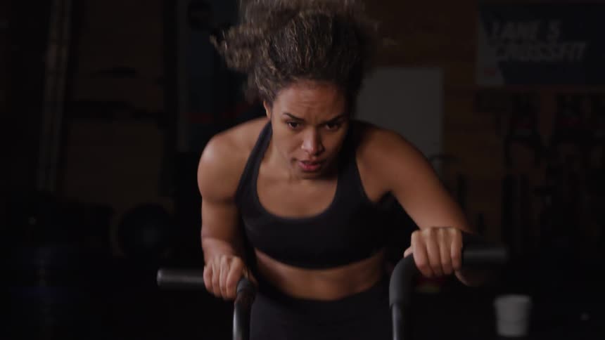 A woman is working out intensely on an air bike at the gym