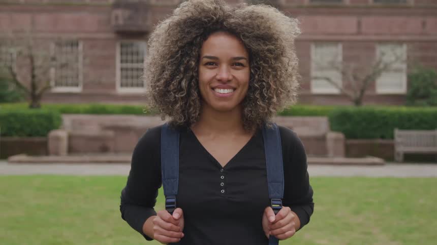 A woman with a backpack stands outside on a college campus