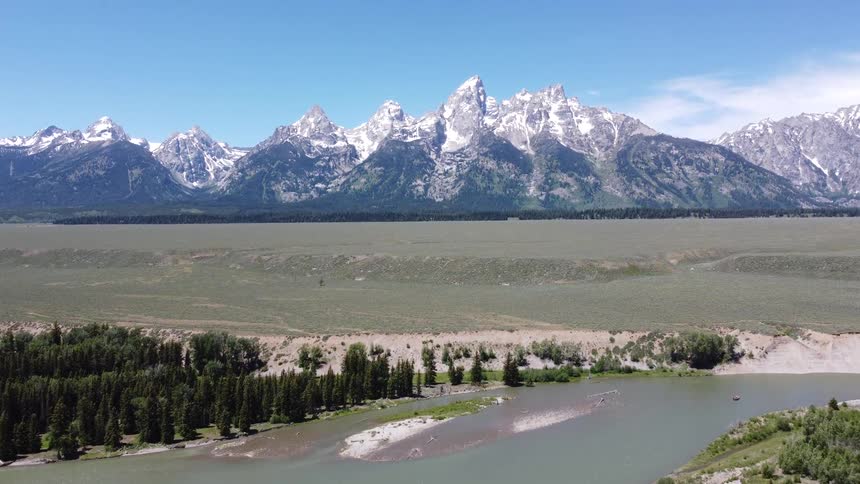 Aerial view of river through valley with forest and snowy mountains