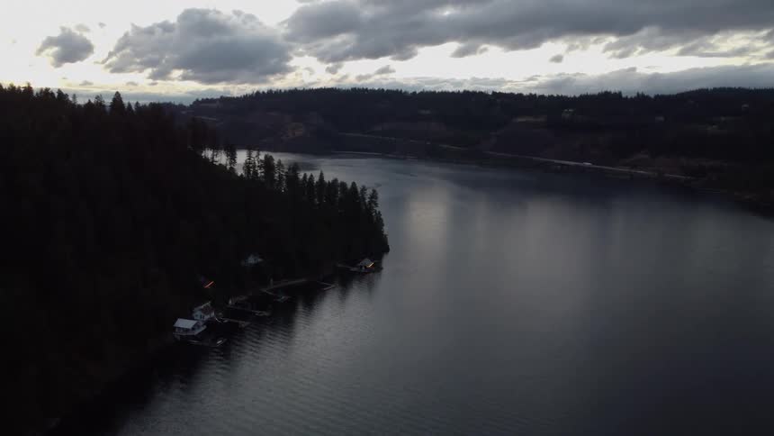 A lake sits under a cloudy sky surrounded by woodland in a rural area