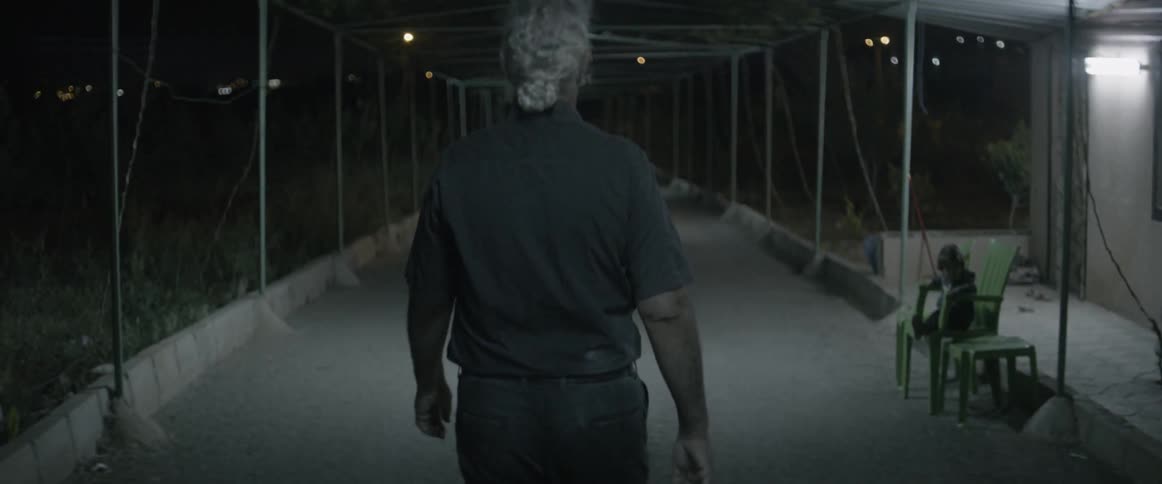 An elderly man walks under scaffolding at night