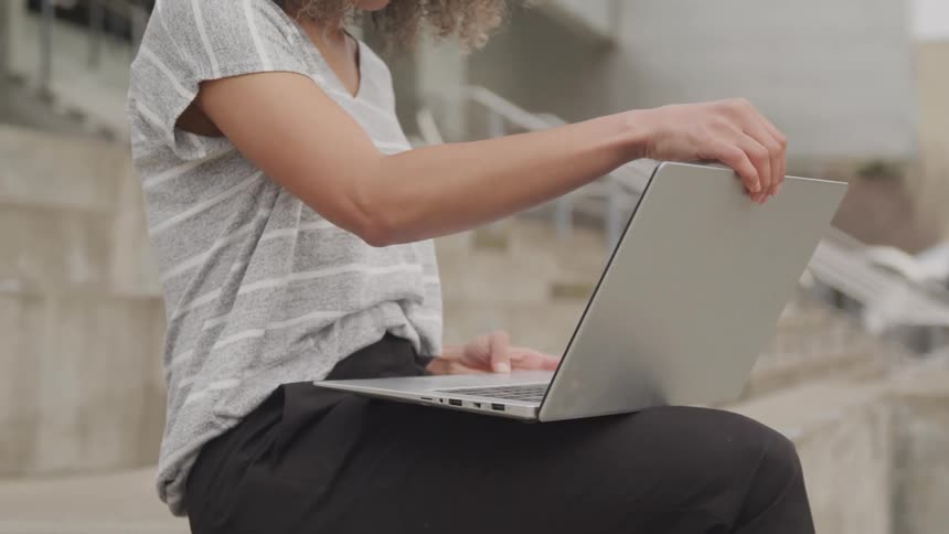 Person sitting on stairs types on a laptop resting on their lap