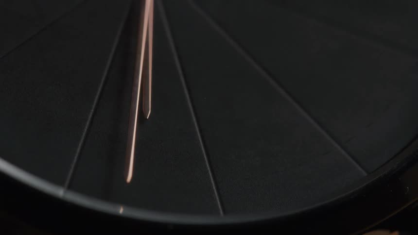 A closeup shot of a wristwatch reveals its sleek dark face with subtle reddishgold accents on the hands and markers the second hand is observed moving smoothly across the watch face