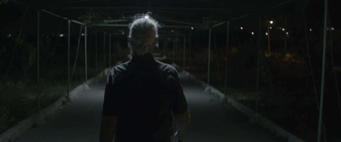 An elderly man walks under scaffolding at night