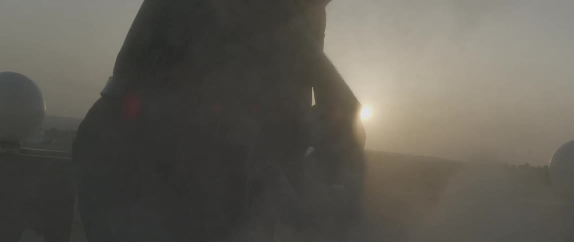 A man uses a power tool to grind a rock as dust flies all around