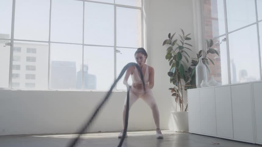 Woman exercises with ropes in a brightly lit room with large windows