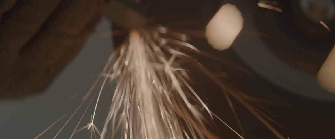 A gloved hand holds metal to a grinding wheel causing sparks