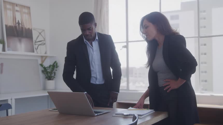 Two workers point at a laptop and talk in the office