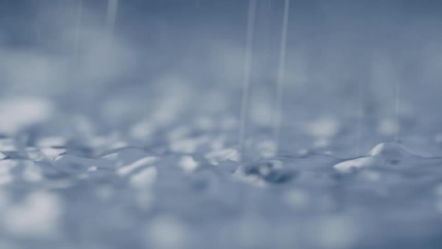 Water bubbles ripple across a smooth surface as rain falls in soft blue light