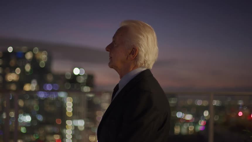 An older man gazes over a city skyline at dusk