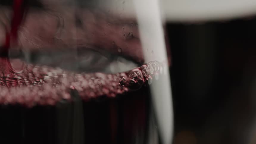 Red wine being poured into a glass showing bubbles forming on the surface as it settles