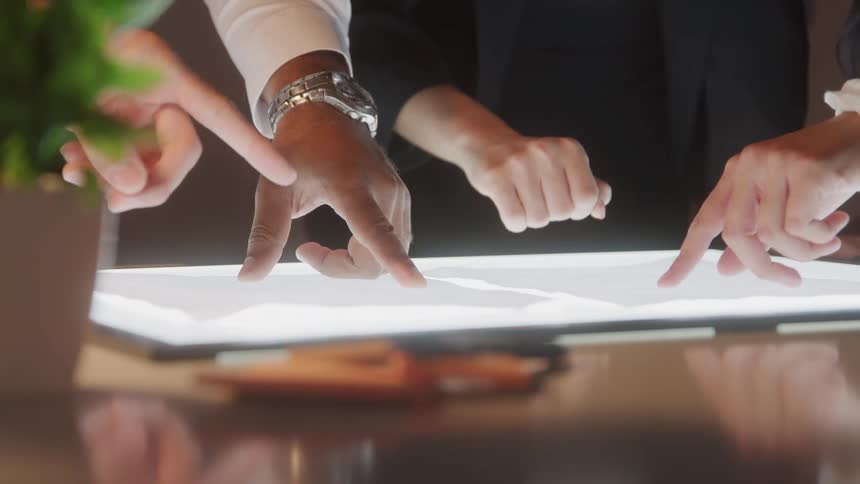 Several hands point and analyze a lit surface together during a meeting