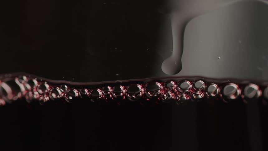Dark red liquid fills a glass forming a neat line of bubbles along the surface