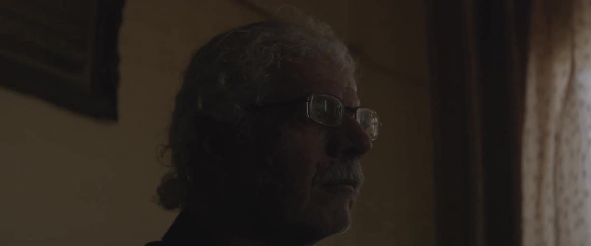 An elderly man ponders in a dim room