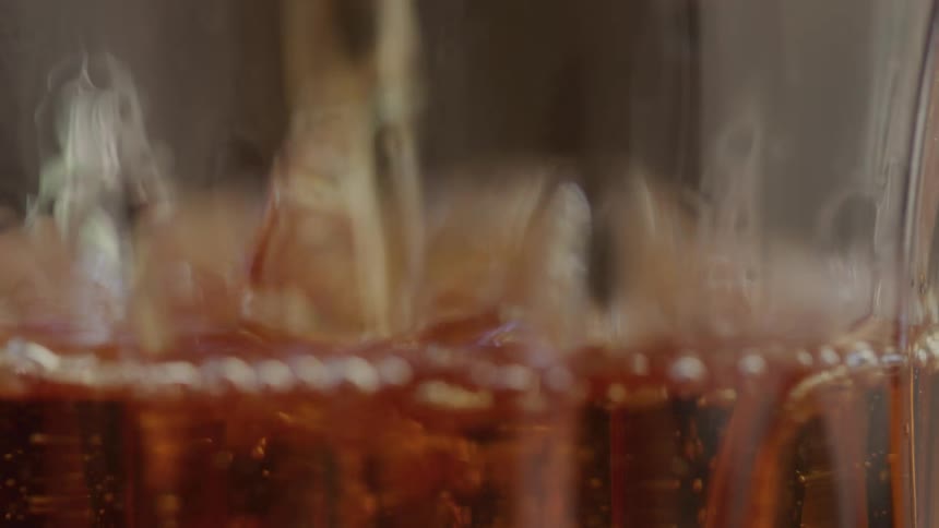 An amber colored liquid is gradually poured into an empty glass