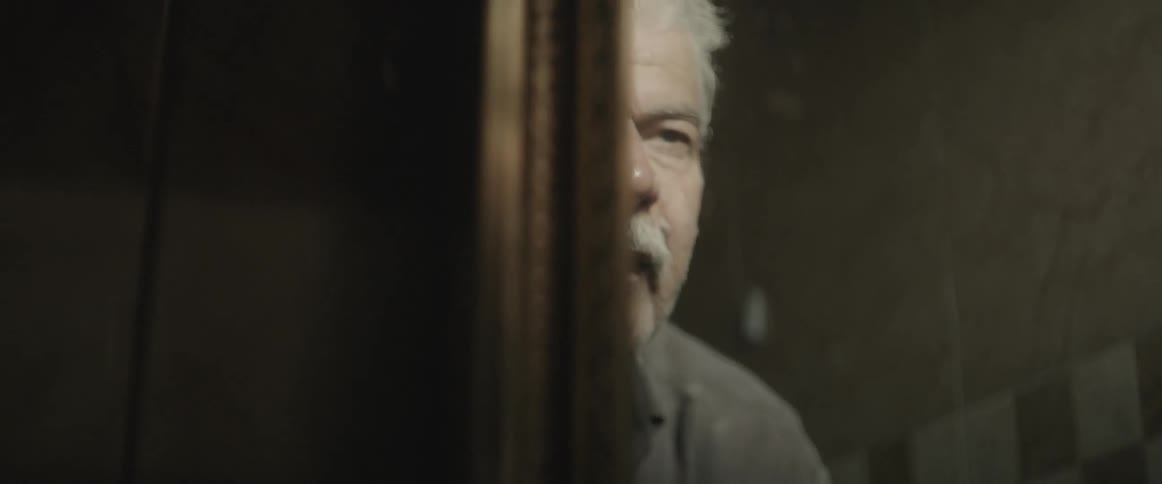 An elderly man washes his face and looks at his reflection