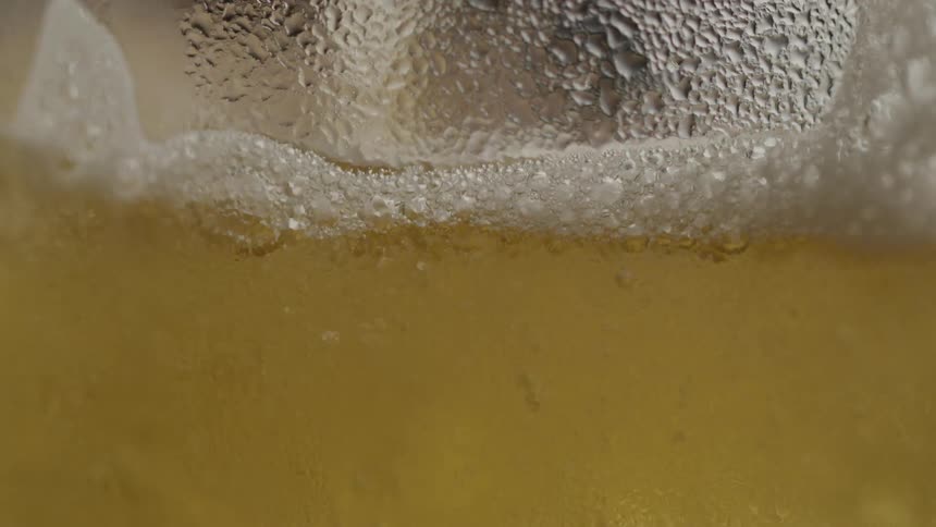 Extreme close up pouring beer as bubbles rise up to top