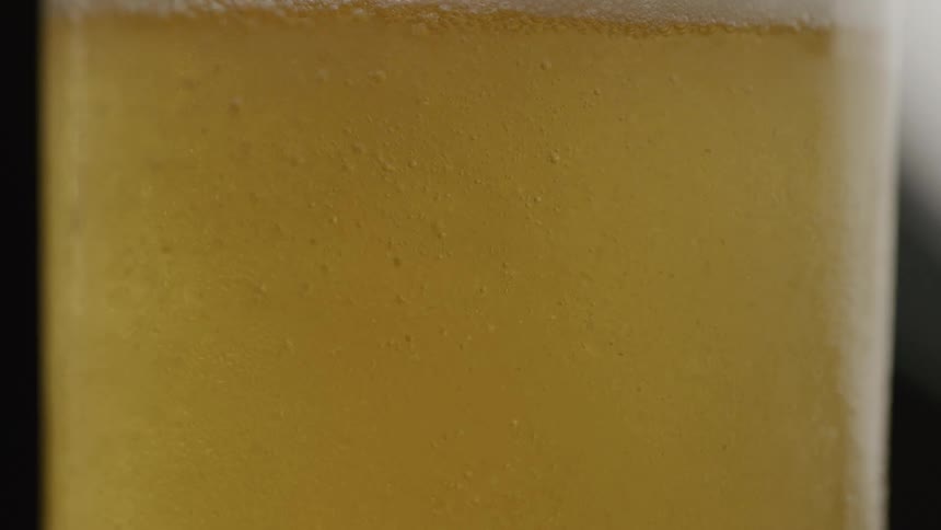 Close up beer being poured with bubbles rising to top of glass