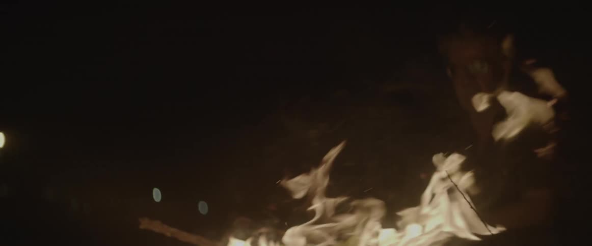 A man sits near an outdoor fire