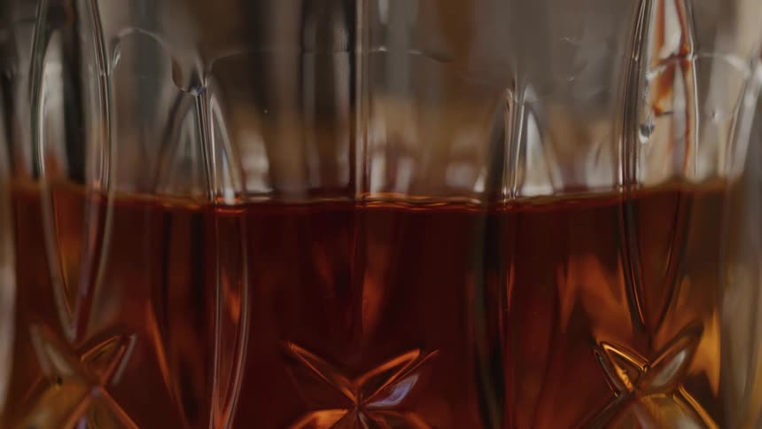 A closeup of amber liquid in a cutglass tumbler softly blurred with warm reflections